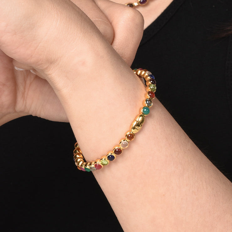 Multicolored gemstones bangle on a person's wrist against a black background
