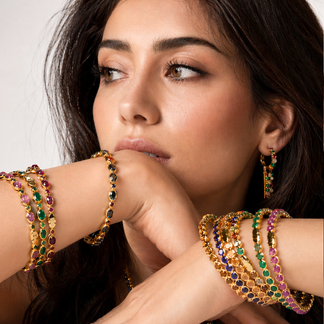 Woman wearing gold plated bangle with gemstones on a neutral background